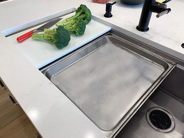 Stainless steel workstation sink designed to hold steam oven pans adjacent to cutting boards.