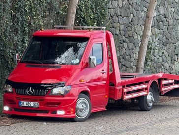 Red Mercedes flatbed tow truck parked on a cobblestone street.