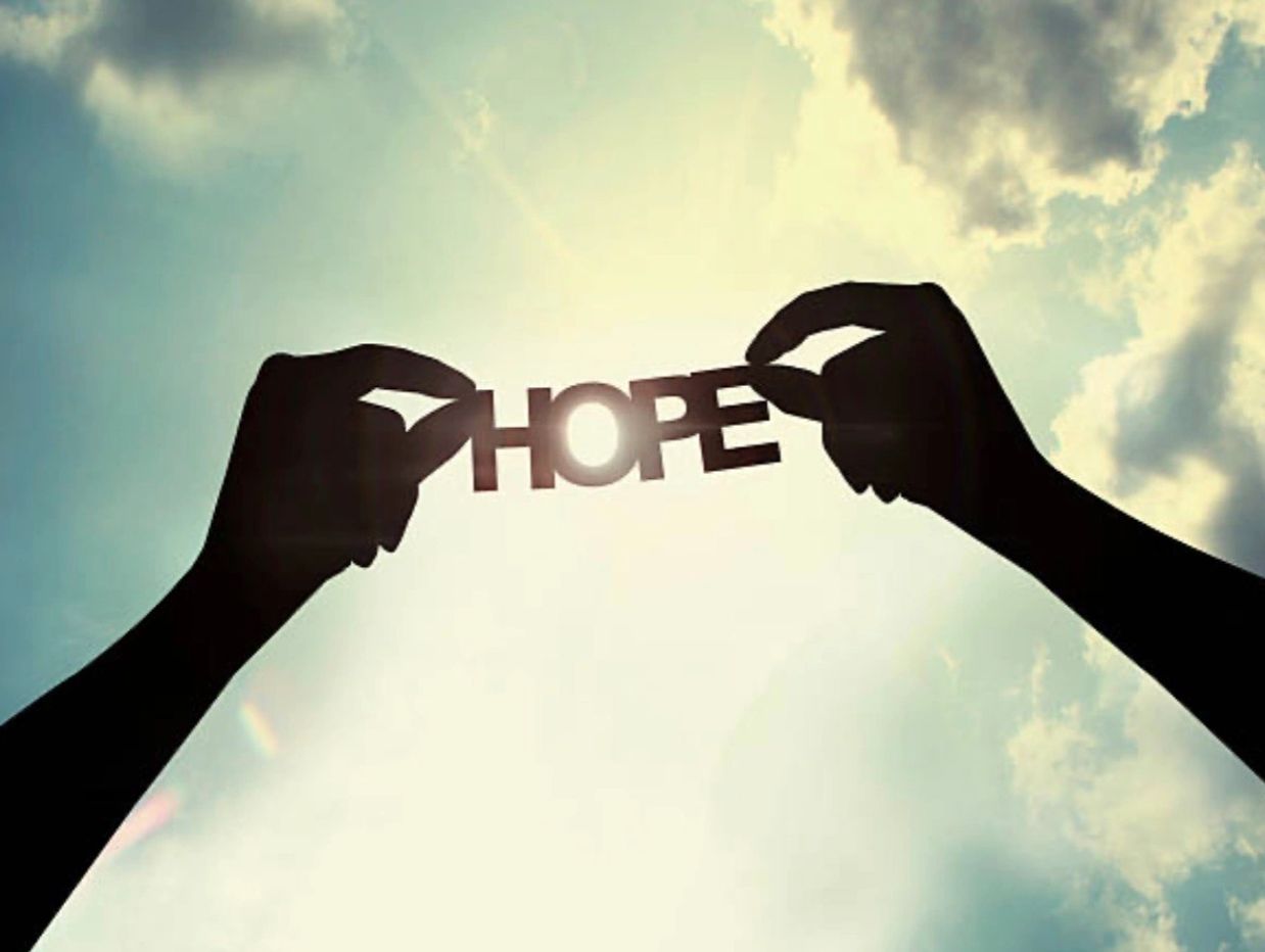 Silhouetted hands holding the word 'HOPE' against a bright sky.