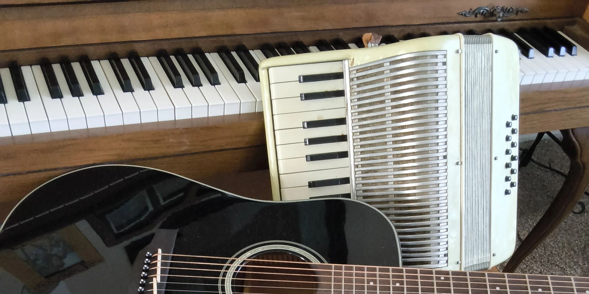 A piano, accordion, and guitar arranged closely together.