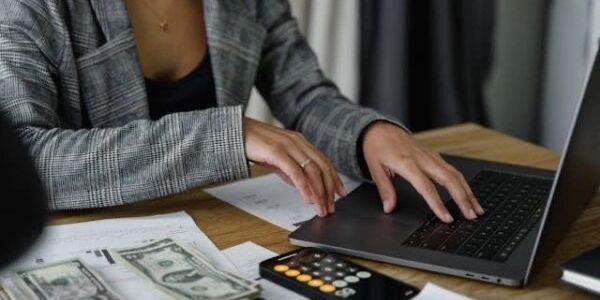 Person working on laptop with money and calculator nearby.