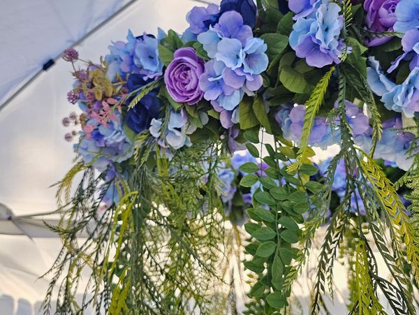 A hanging floral arrangement with purple and blue flowers under a white canopy.