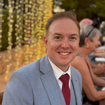 Man in a light blue suit and red tie smiling at an outdoor event.