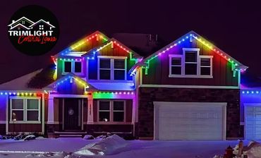 A home with a rainbow patterned Trimlight system amidst a snowy Christmas setting.