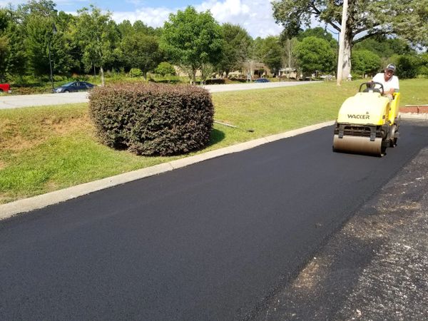 Man operating a yellow Wacker roller on freshly paved asphalt.
