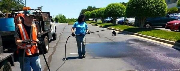Two workers sealing a road with asphalt on a sunny day.