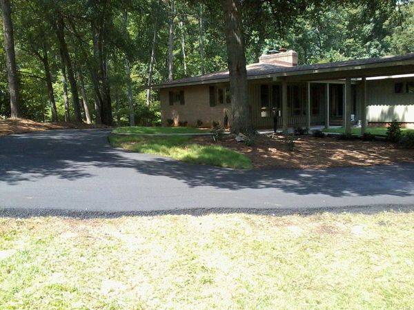 A house surrounded by trees with a freshly paved driveway.