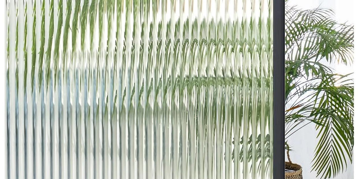 Decorative textured glass panel with a black metal frame and green plants behind.