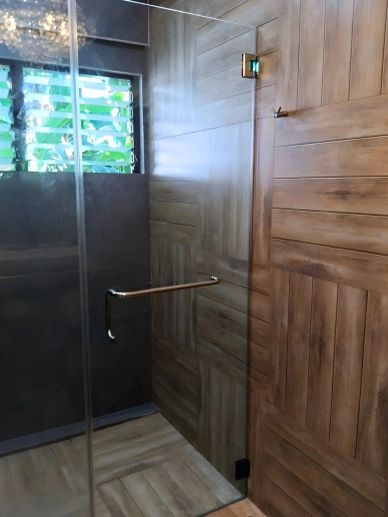 Modern shower with wooden panels and glass door in a bathroom.