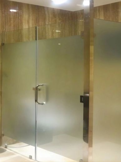 Modern frosted glass shower door with metal handle in a marble bathroom.