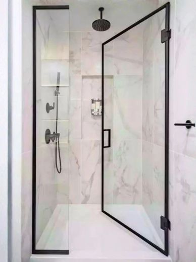 Modern glass shower enclosure with black frames and marble walls.