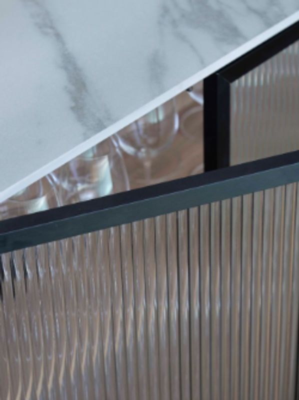 Close-up of a marble countertop and textured glass cabinet door with glassware inside.
