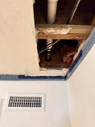 Ceiling hole reveals pipes and insulation in a room corner.