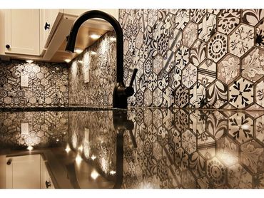 Kitchen sink area with patterned hexagonal tile backsplash and glossy countertop reflection.