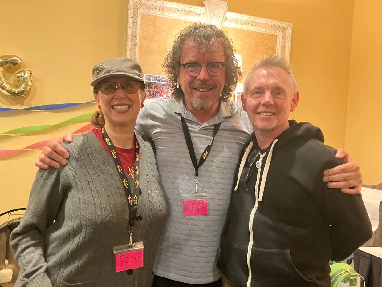 Three friends smiling and posing together indoors at a casual event.
