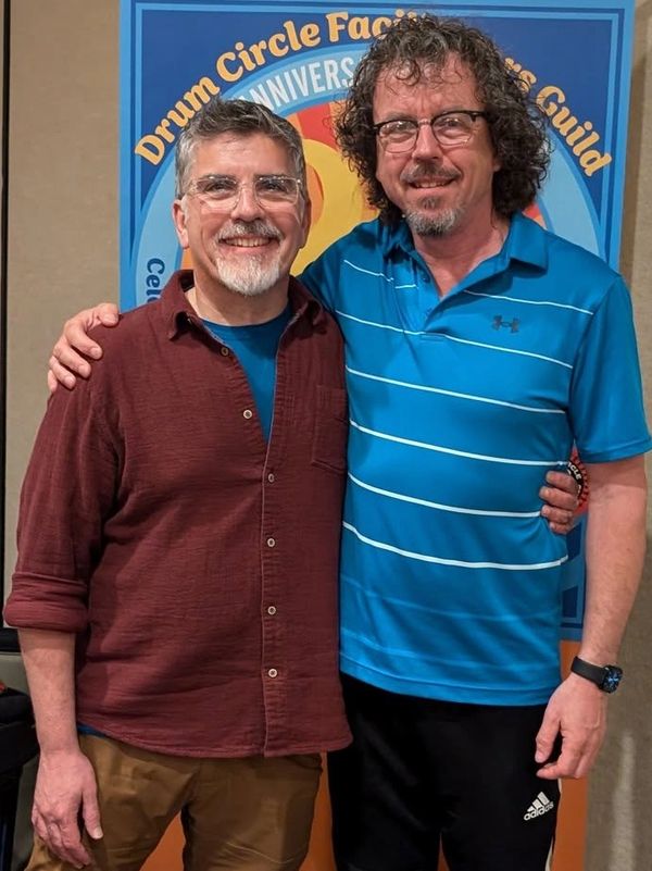 Two men smiling and posing together in front of a colorful banner.