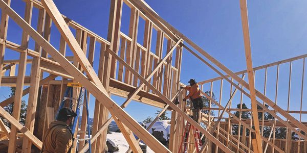 Construction workers framing a wooden house under clear blue sky with snow outside.