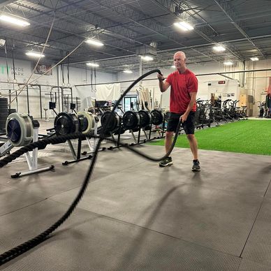 Man in red shirt exercising with battle ropes in a gym.