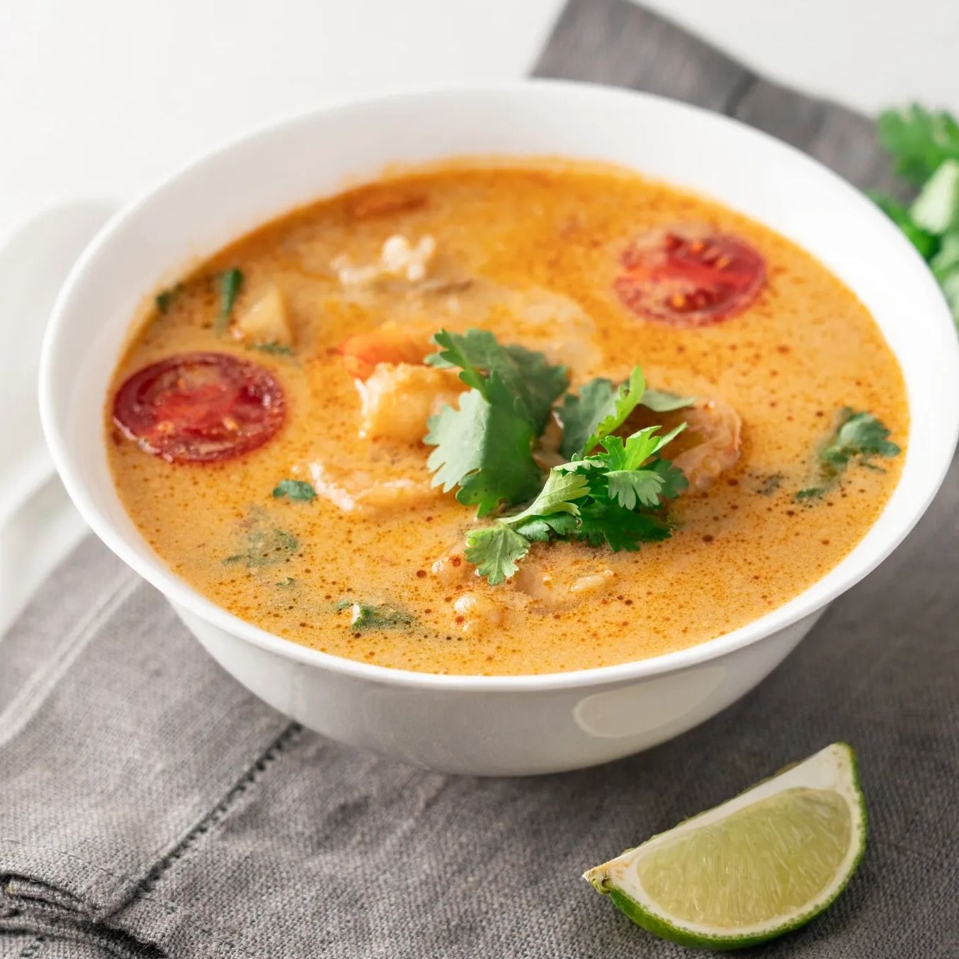 A bowl of creamy spicy shrimp soup garnished with cilantro and tomato slices.