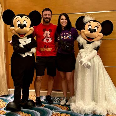 Couple posing with Mickey and Minnie Mouse characters indoors.