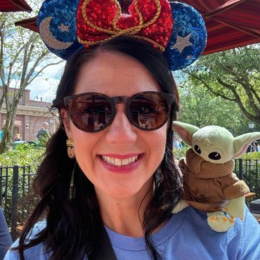 Smiling woman wearing Mickey ears and Baby Yoda plush on her shoulder.