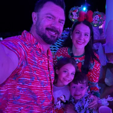 Family selfie with festive Mickey-themed attire under purple lighting.