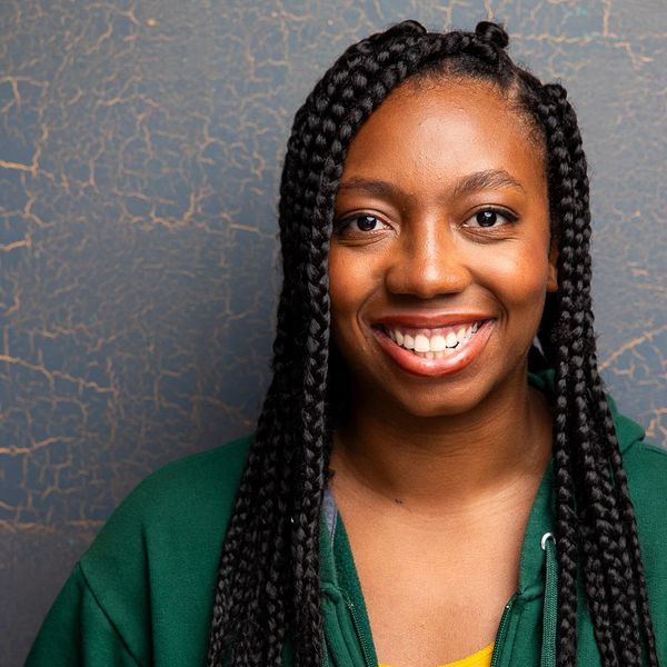 Smiling woman with long braids and green hoodie.