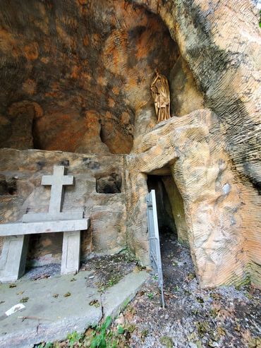 A stone cross and statue inside a rocky cave shrine.