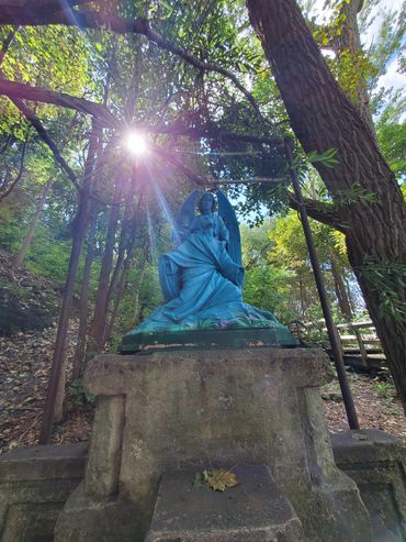 A blue angel statue in a sunlit forest setting.