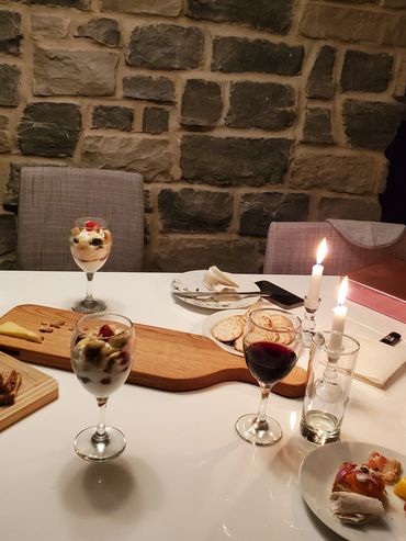 A cozy dinner setup with wine, desserts, and lit candles.