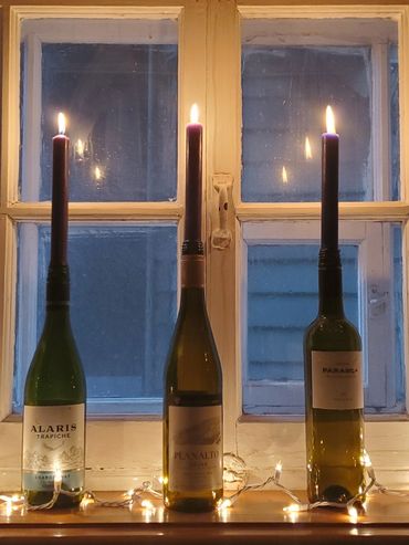 Three wine bottles with lit candles inside them on a windowsill at dusk.