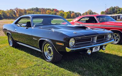Classic black muscle car parked on grass with a red car beside it.