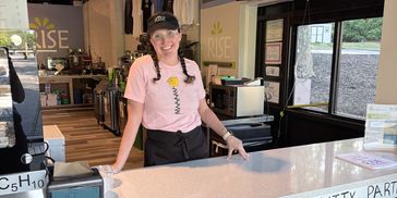 Smiling barista stands behind the counter at Rise café.