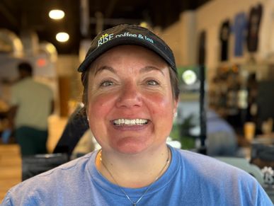Smiling woman wearing a black visor and blue shirt in a cozy cafe.
