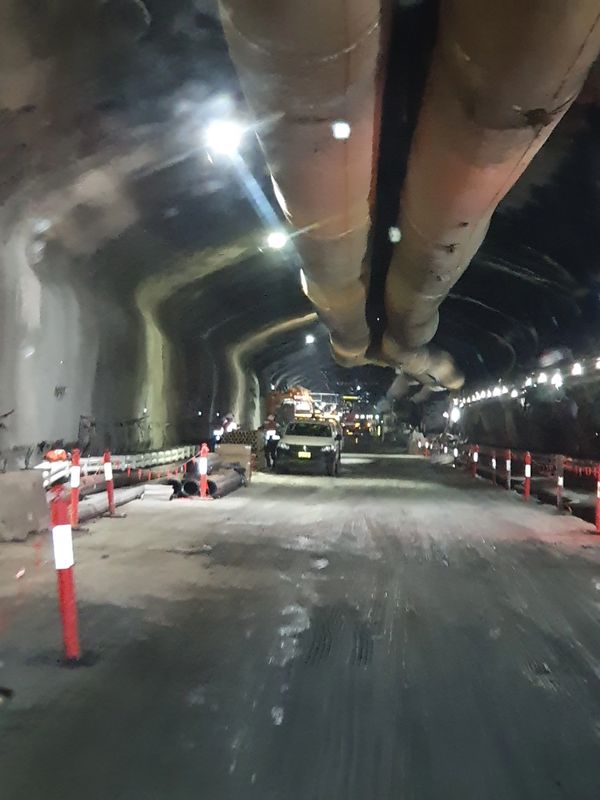 Construction work inside a dimly lit tunnel with vehicles and safety barriers.