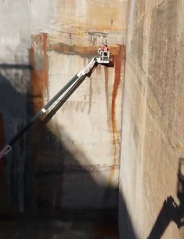 Worker on a lift platform cleaning or inspecting a large concrete wall.