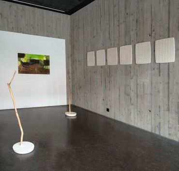 Plaster casts on a concrete wall, with a green painting and two sculptures made with wood and plaste