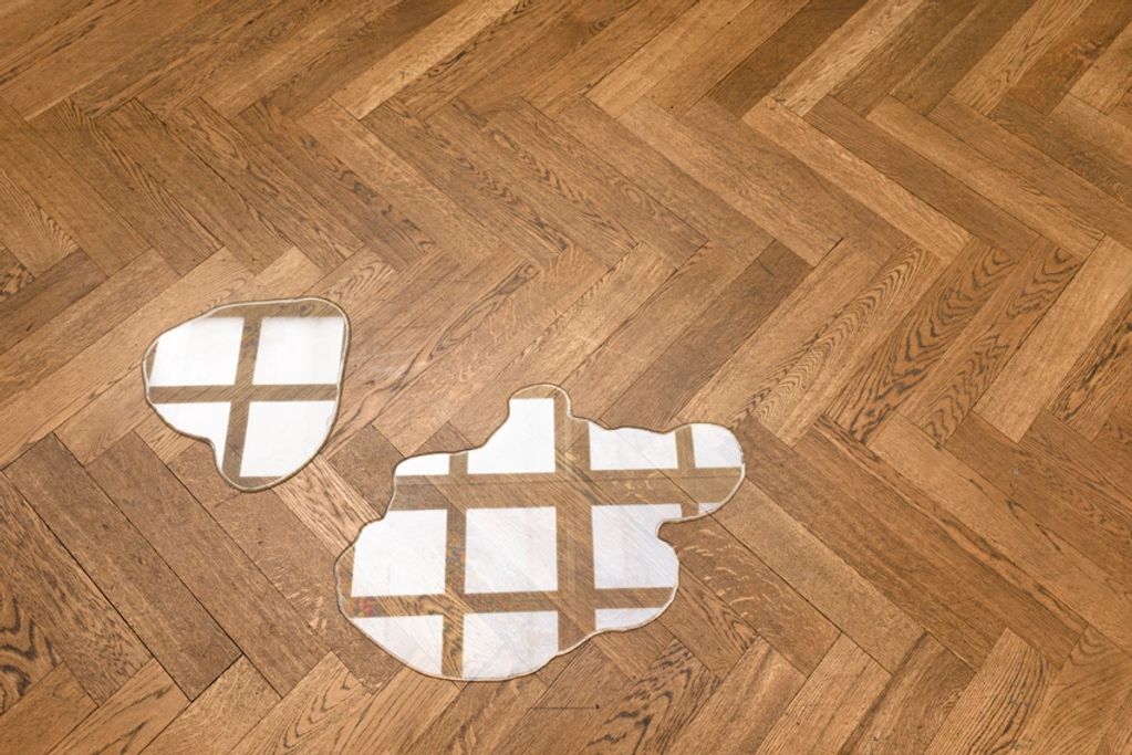 Two puddle-shaped mirrors on a wooden floor.
