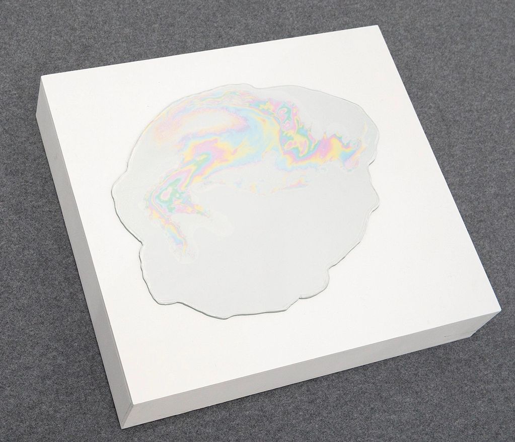 White block with an iridescent, water-like shape on top.