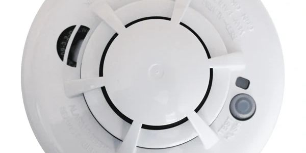 Close-up of a white smoke detector with vents and a test button.