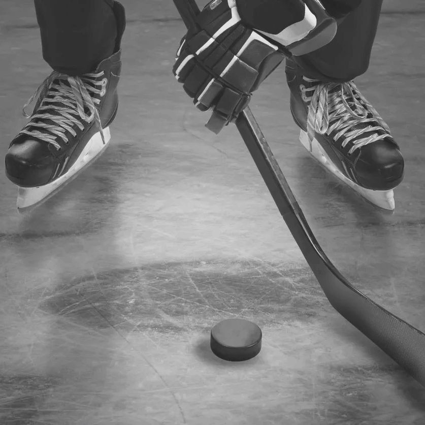 Close-up of hockey player with skates, stick, and puck on ice rink.