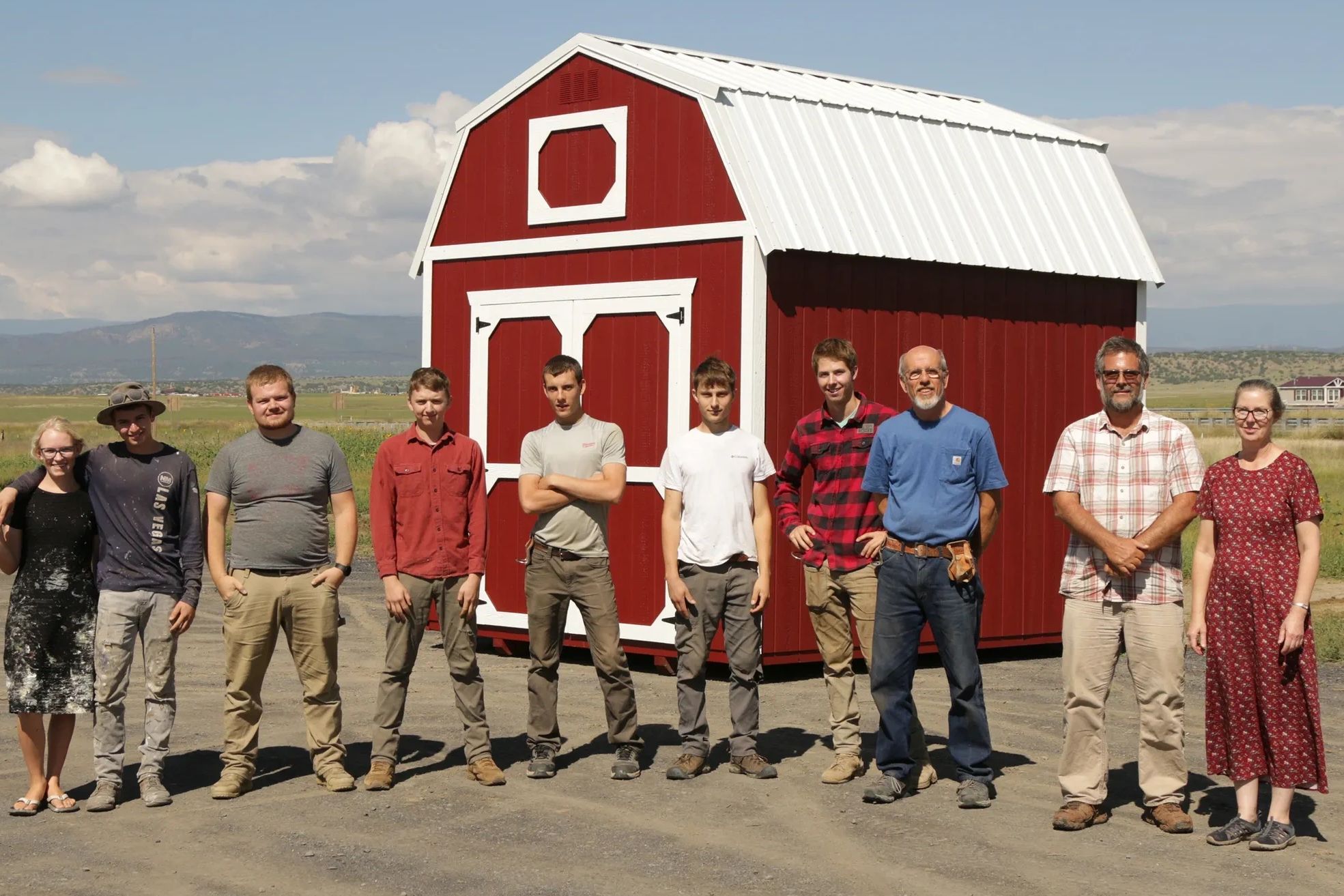 Team standing in front of red shed with white trim – American Barn Co staff and builders photo