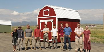 Team standing in front of red shed with white trim – American Barn Co staff and builders photo