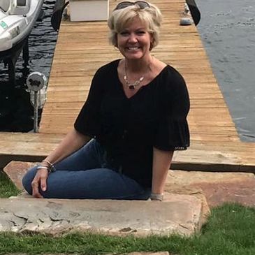 A woman sitting on a stone by a wooden dock with a jet ski nearby.