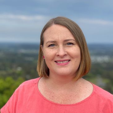 Woman in pink shirt smiling with a scenic background.