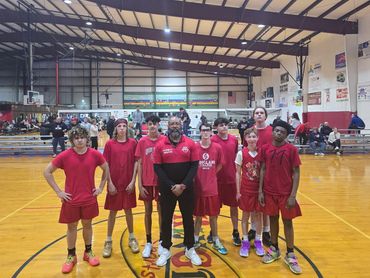 Youth basketball team posing with their coach in an indoor gym.