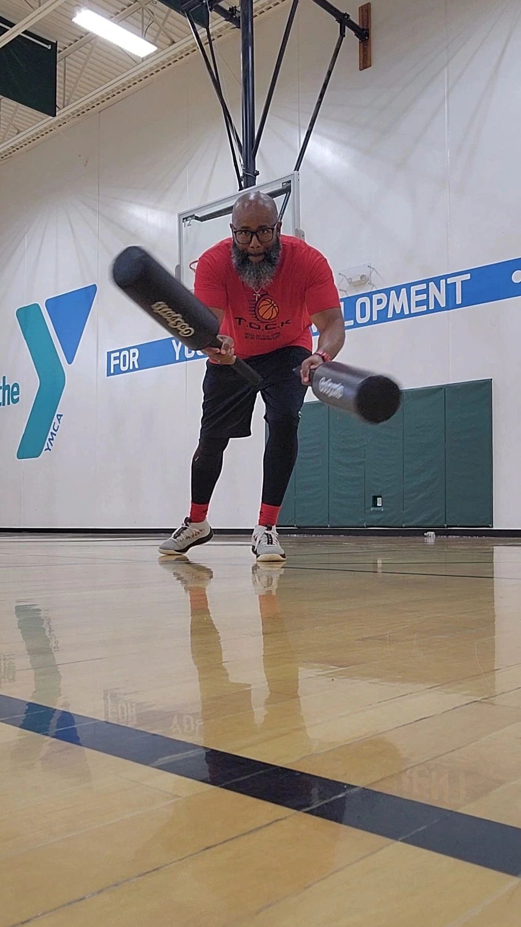 Man practicing baseball swings in a gym with two bats.