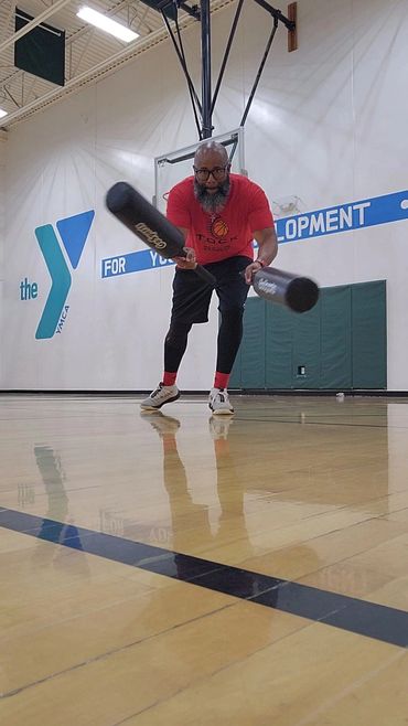 Man practicing baseball swings in a gym with two bats.