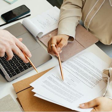 Two people reviewing documents and pointing with pens near a laptop.