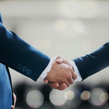 Two people in suits shaking hands in a professional setting.